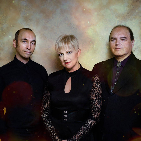 A formal portrait of the band Autumn, featuring three members in elegant dark attire against a soft textured background