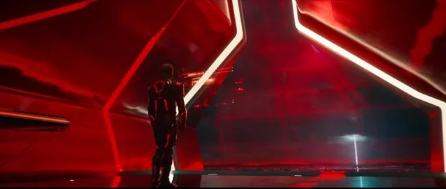 A figure stands before a massive red digital chamber inside the new Grid, surrounded by towering geometric light.
