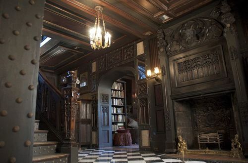 Interior of a dark, wood-paneled historic house with a staircase, bookshelves, and multiple visible pathways, suggesting exploration and depth.